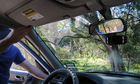 Messy DIY dash camera install with dangling power cable and suction cup mount blocking windshield view — unprofessional installation example